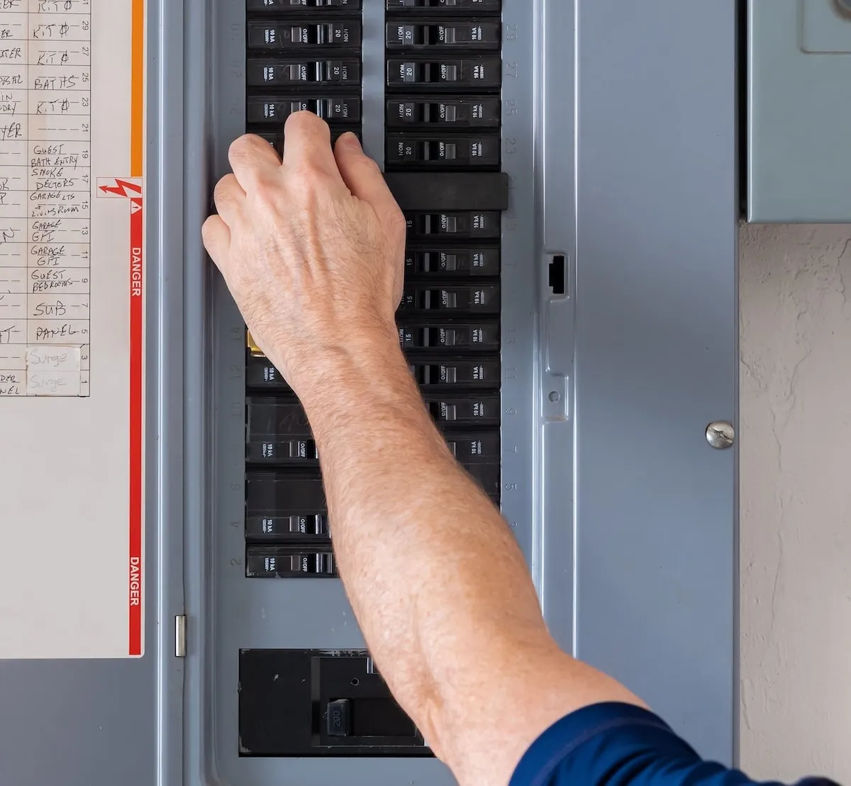 Person's hand adjusting a circuit breaker switch inside a gray electrical panel.